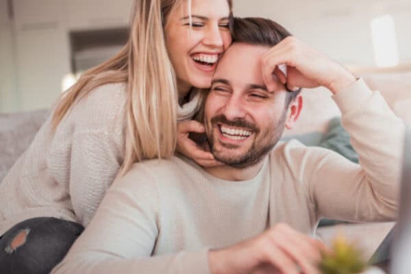 A happy couple sitting on a couch in a cozy living room, laughing and enjoying each other's company.