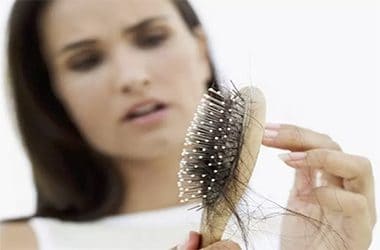 A woman looking concerned as she examines hair caught in a hairbrush, highlighting hair loss.