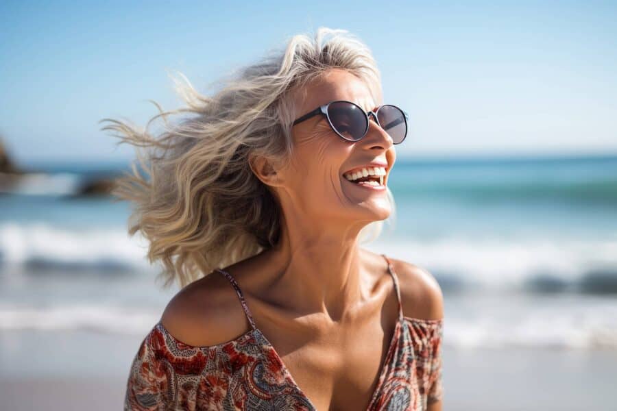 A mature woman smiling in the sun on a beach near the ocean