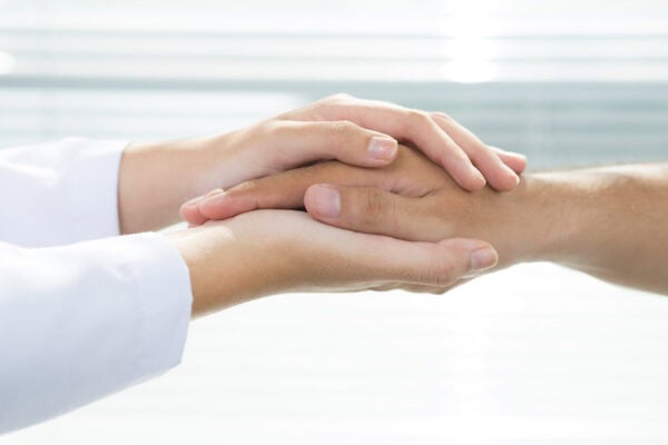 Close-up of two hands clasped together in a gesture of support and compassion, with a bright, soft background.