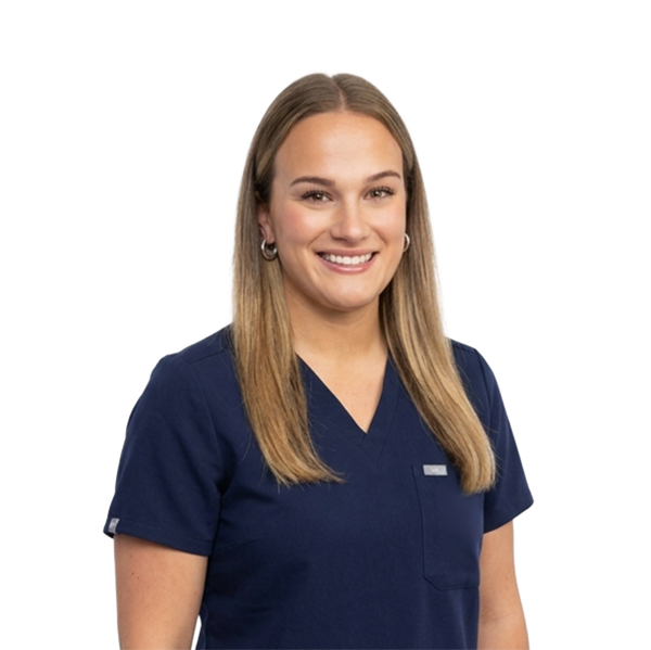 A woman with long brown hair and glasses, smiling while wearing blue scrubs against a white background.