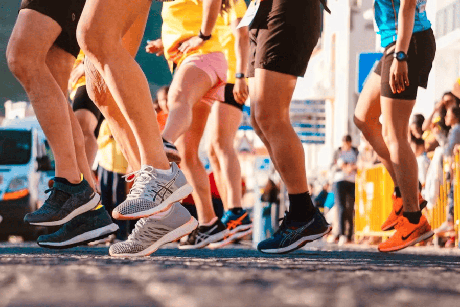 Close-up of runners' legs and shoes at the starting line of a race, with a colorful and energetic outdoor atmosphere.