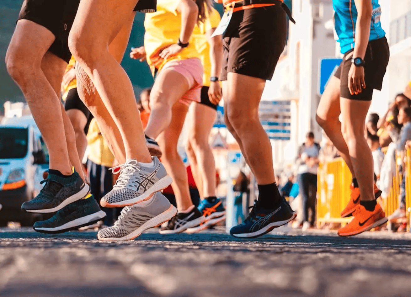 Close-up of runners' legs and shoes at the starting line of a race, with a colorful and energetic outdoor atmosphere.