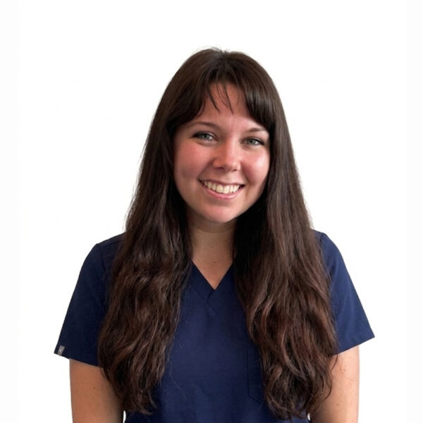 A woman with long brown hair and glasses, smiling while wearing blue scrubs against a white background.