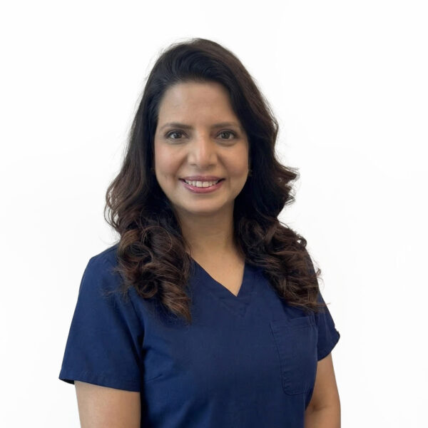 A woman with medium-length brown hair, wearing a purple top and smiling, standing in front of a white background.