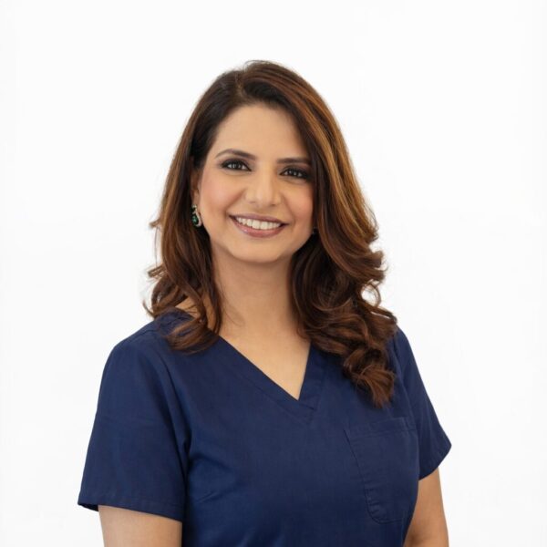 A woman with medium-length brown hair, wearing a purple top and smiling, standing in front of a white background.