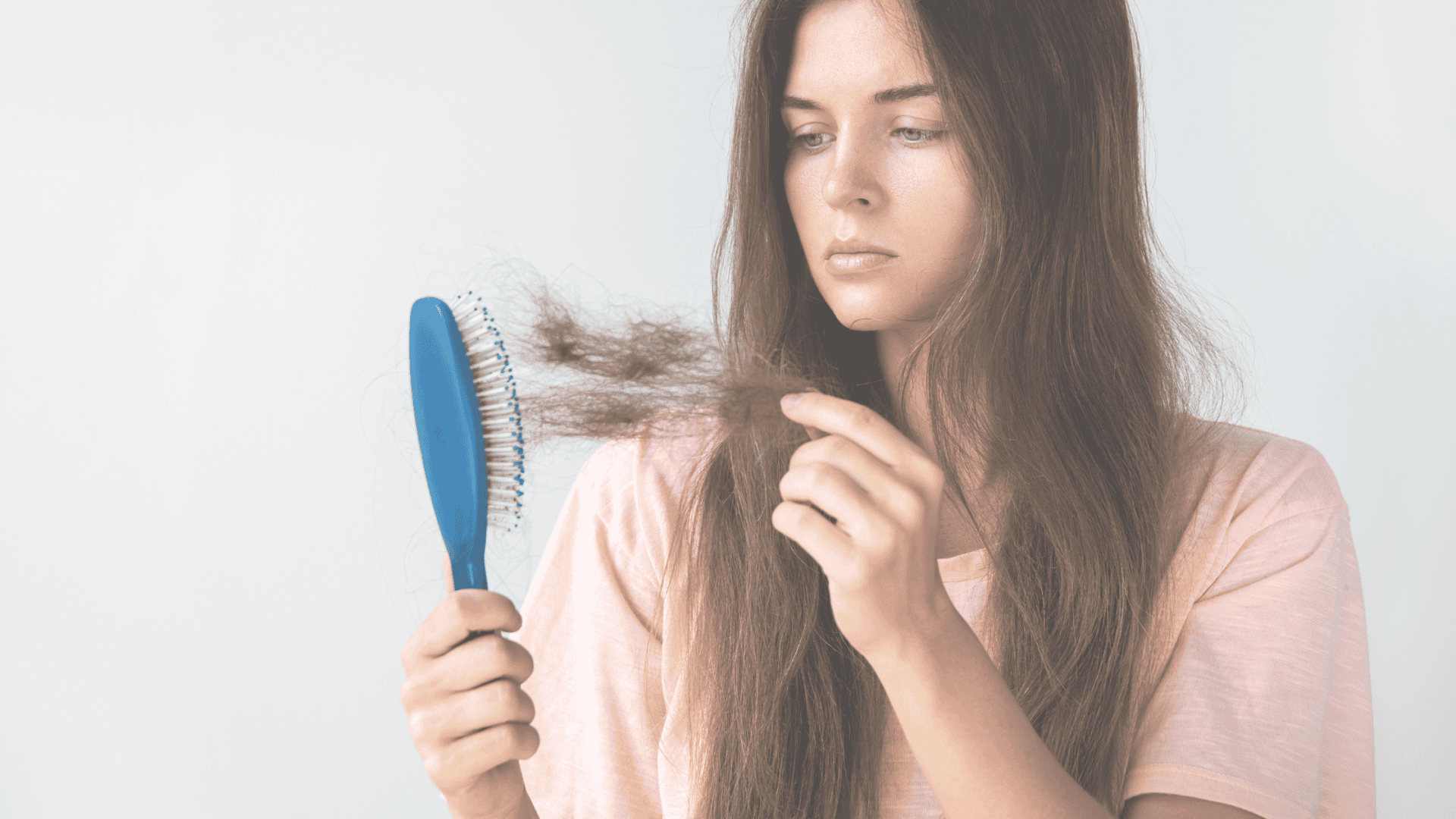 A woman looking concerned as she examines hair caught in a hairbrush, highlighting hair loss.