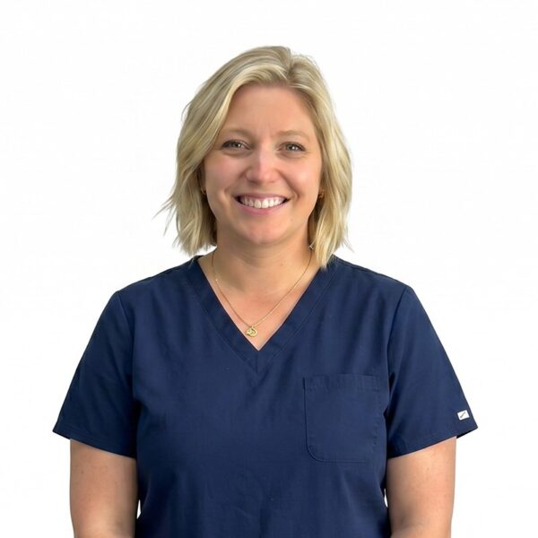 A woman with long brown hair and glasses, smiling while wearing blue scrubs against a white background.