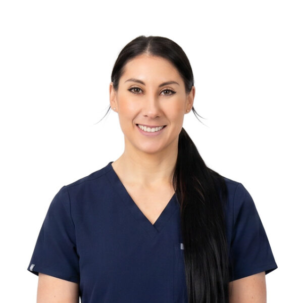 A woman with long brown hair and glasses, smiling while wearing blue scrubs against a white background.