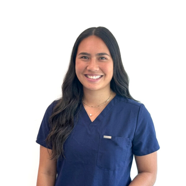 A woman with long brown hair and glasses, smiling while wearing blue scrubs against a white background.