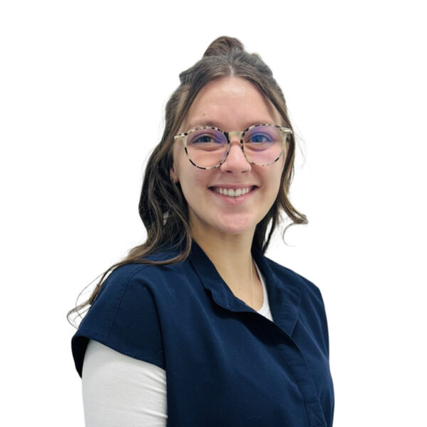A woman with long brown hair and glasses, smiling while wearing blue scrubs against a white background.